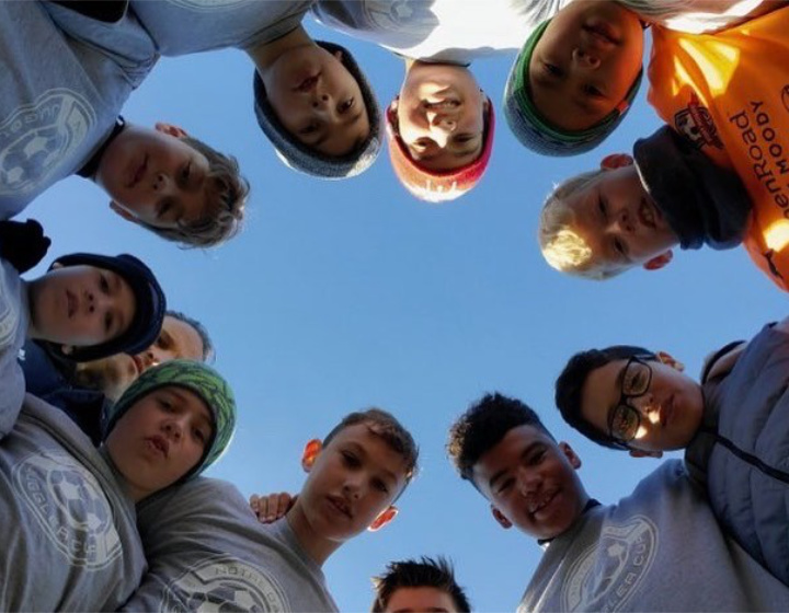 secondary students forming a circle looking down at a camera