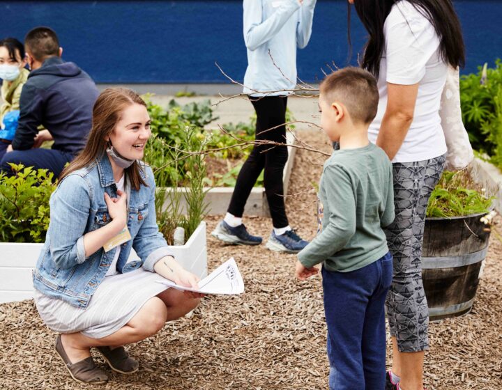 Teacher kneeling down in an outdoor garden speaking to an elementary school aged child