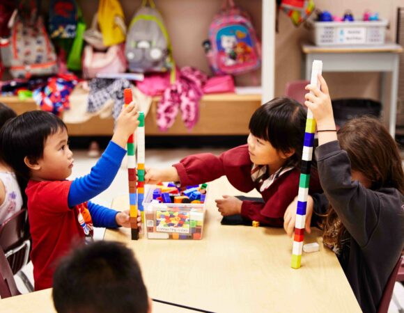 Three primary student playing with connecting cubes at a shared desk.