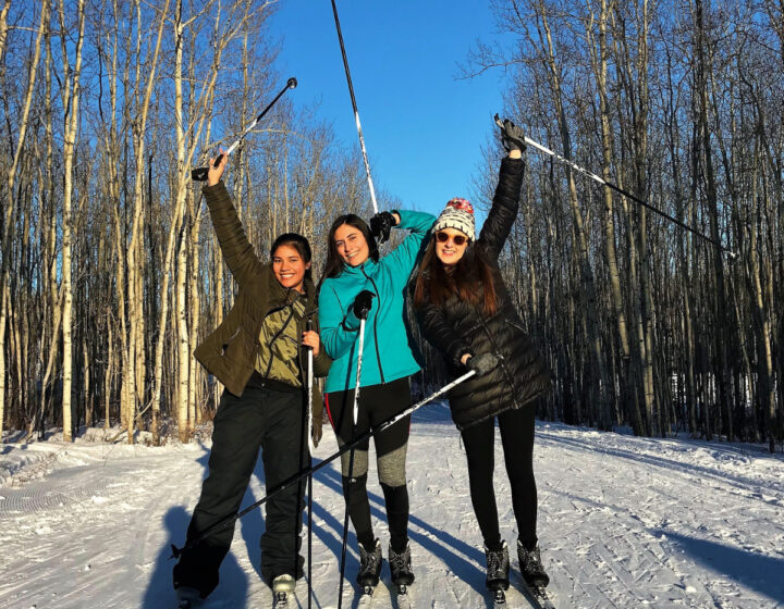 Three School District 60 students cross country skiing on a snowy path in the forest