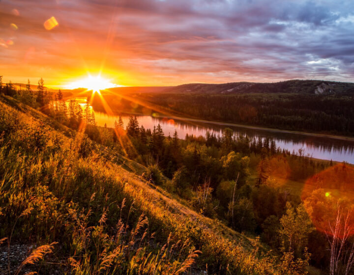 Evening sun setting behind forested mountains along the peace river